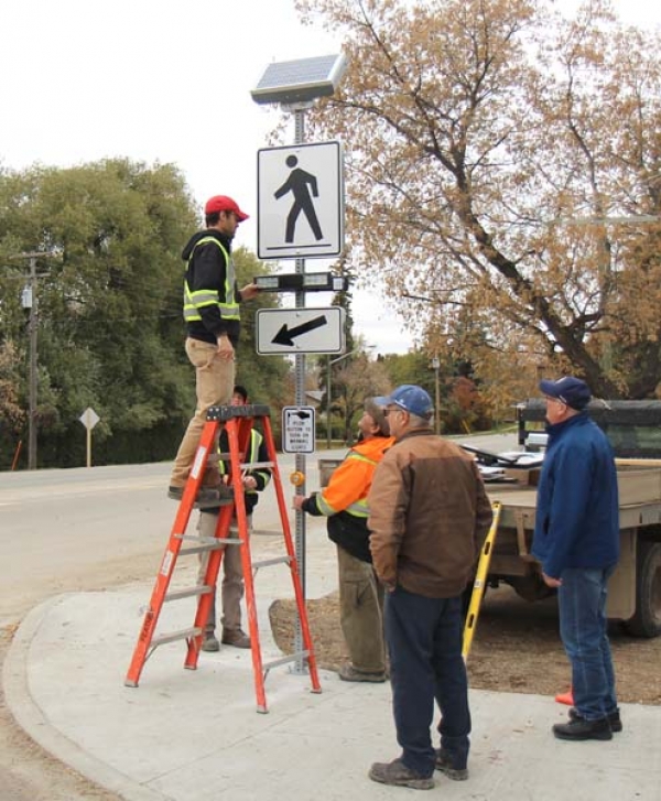 A new crosswalk lighting system was inaugurated at the corner of Mill Road and North Railway St. on Tuesday, October 9. A concerned citizen felt the busy intersection needed to be improved. Municipal council responded with a push-button flashing light that will alert motorists to the need to stop for pedestrians needing to cross. They have approached service clubs in the community to help with the costs. Town of Boissevain employees Dustin Pugh (on ladder), Bryce Adams and Wayne McCallum put up the sign while Mayor David Stead and Councillor Rob Adams inspect.   