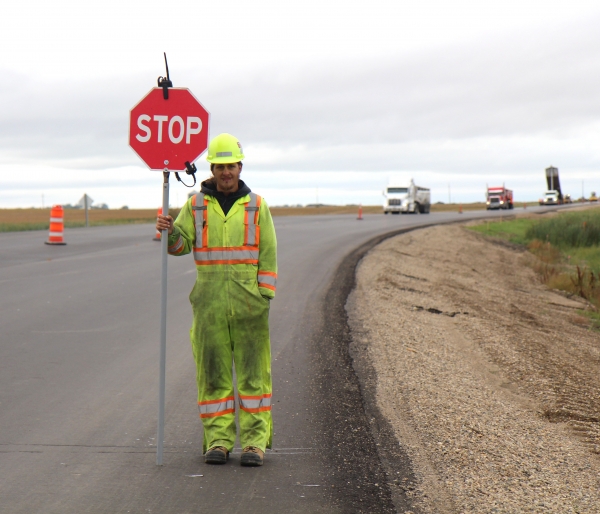 Keith Thorburn of Direct Traffic stops motorists at the curves north of Boissevain, as construction continues on the last phase of the local #10 Highway project. The sign and flag people, who help keep traffic moving while workers do their job, work 12-16 hour shifts, getting 15 minute breaks periodically throughout the day. To avoid drowsy moments and for traffic safety, workers are not given chairs to rest on,  long hours of standing are a matter of course. Thorburn said that the job brings some frustrated comments by travellers, but other times people are sympathetic and have even dropped off some cold drinks on hot days. Thorburn has been with the company since June, working in different areas around the province.  